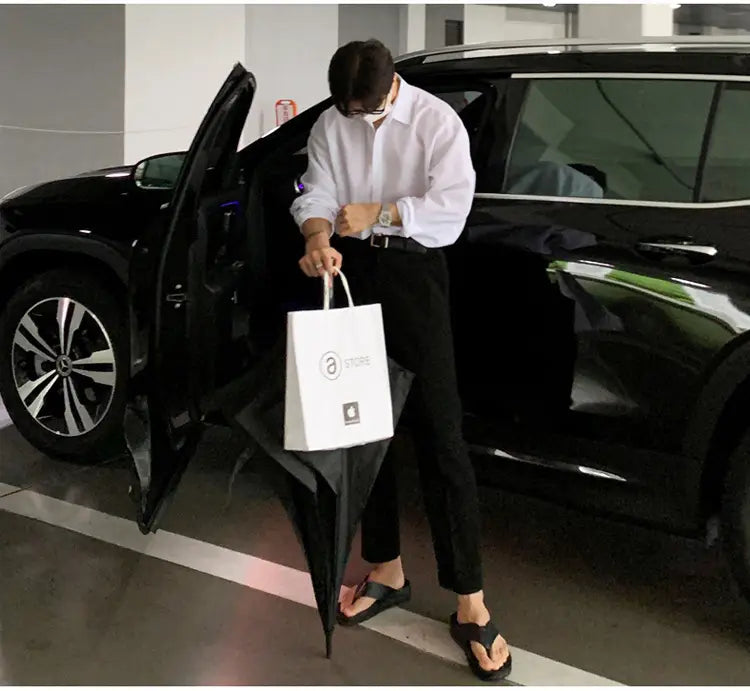White paper shopping bag with a minimalist logo and sturdy handles alongside a men black long sleeve casual button down shirt.