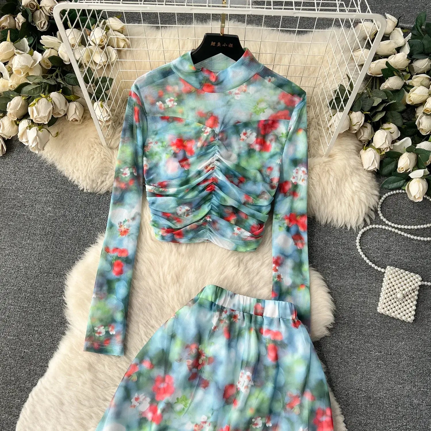 Two piece mesh skirt set with a marble print elastic closure featuring a long sleeved high neck top with ruched waist and matching floral skirt in soft blue red and green hues.