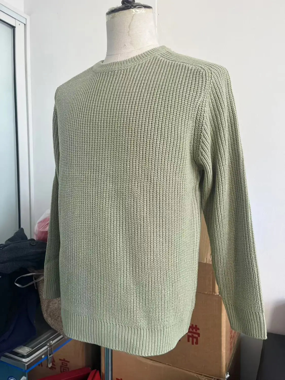 ein weicher, salbeigrüner Rippstrick-Chunky-Strickpullover für Herren mit klassischem Crewneck und langen Ärmeln, auf einer Schaufensterpuppe für einen lässigen Look präsentiert