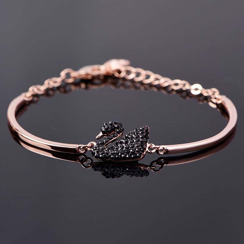 Bracelet jonc à tonalité or rose, présentant une breloque de cygne sertie de cristaux noirs.