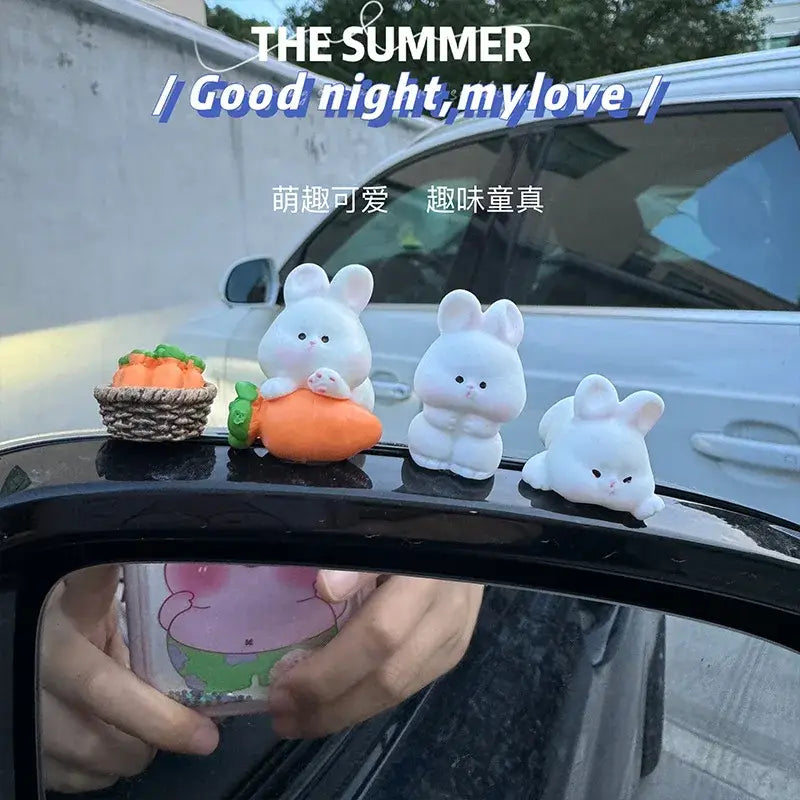 Trois adorables ornements de tableau de bord de voiture en peluche en forme de lapin blanc, avec des expressions mignonnes, assis sur un rétroviseur de voiture.