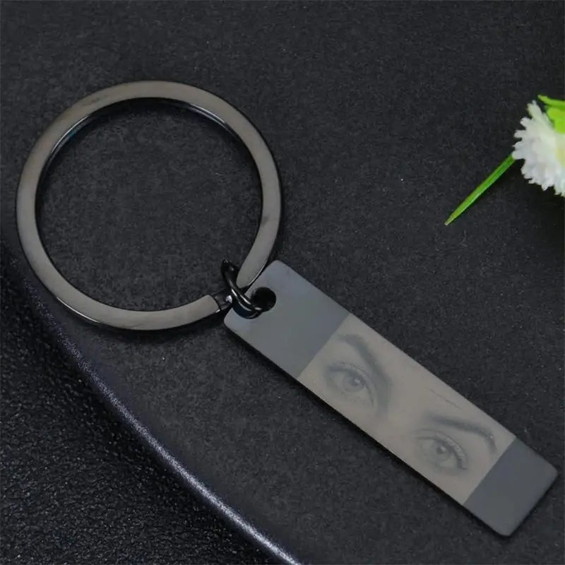 Black metal keychain with a rectangular stainless steel tag featuring a custom engraved close-up of eyes for personalized use.
