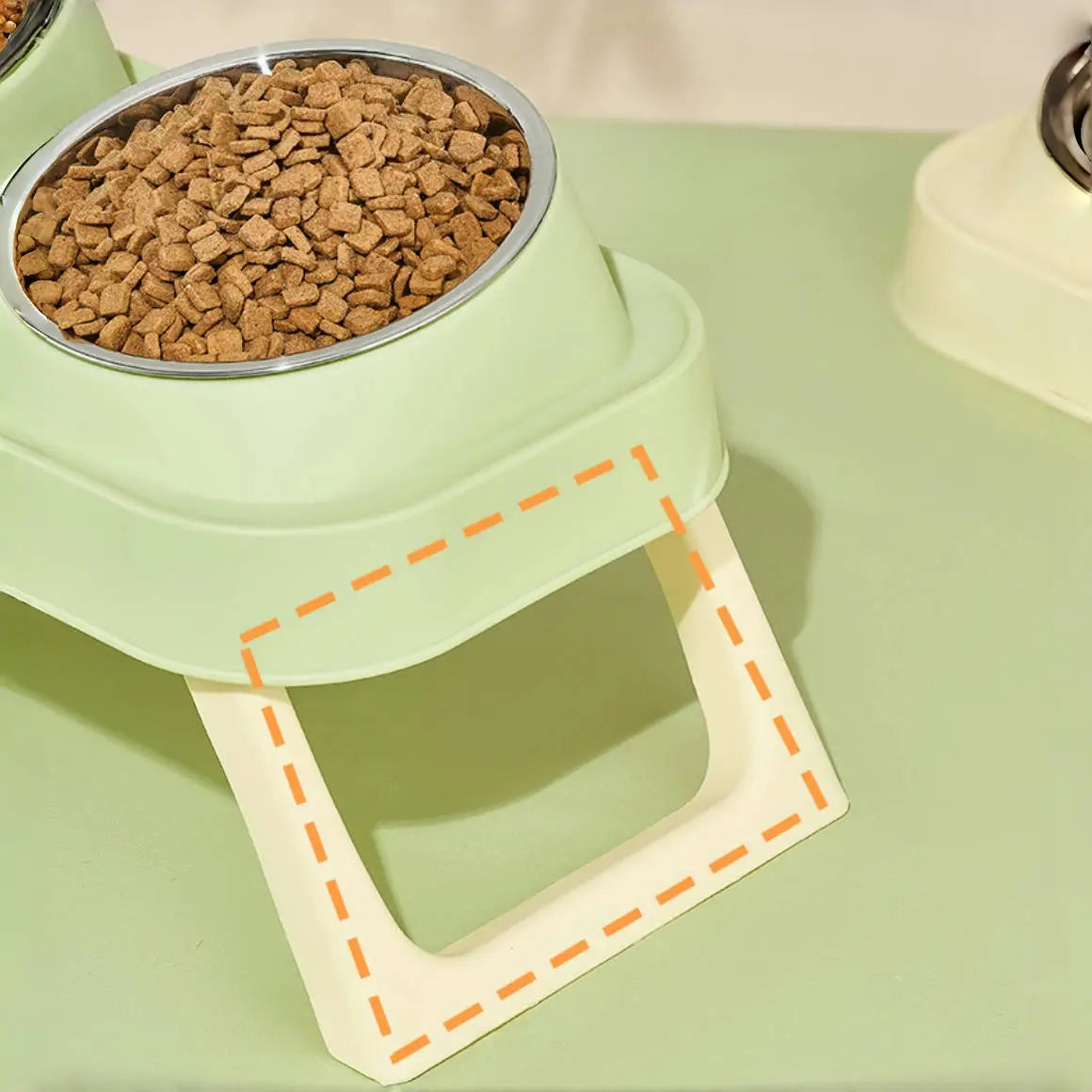 Light green plastic pet food bowl with a silver rim filled with brown kibble in an elevated stainless steel pet feeder with tilt bowls.