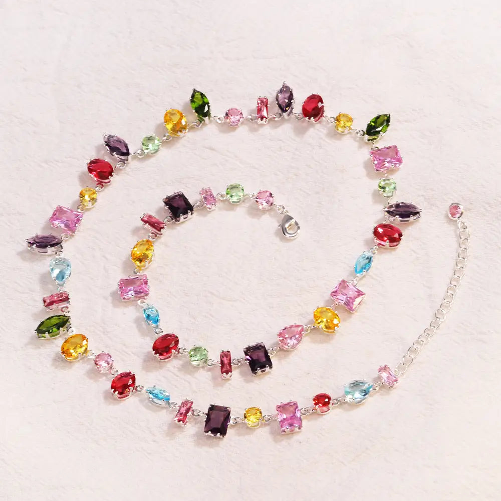 A colorful zircon crystal gold plated necklace featuring a silver chain and assorted faceted gemstones in shades of pink red yellow green blue and purple.