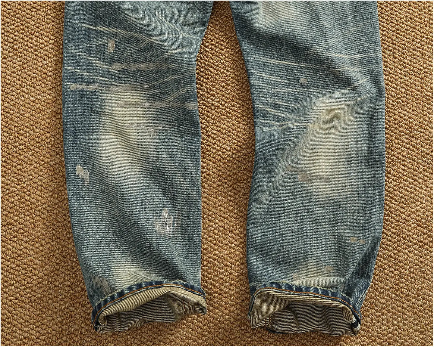 Distressed patchwork denim jeans for men in blue featuring faded patches and whiskering on cotton material.