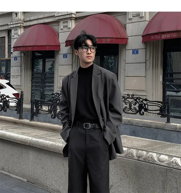 Un hombre que lleva una blazer de doble botonadura oversize de poliéster gris oscuro con pantalones negros y cuello vuelto negro para uso casual.
