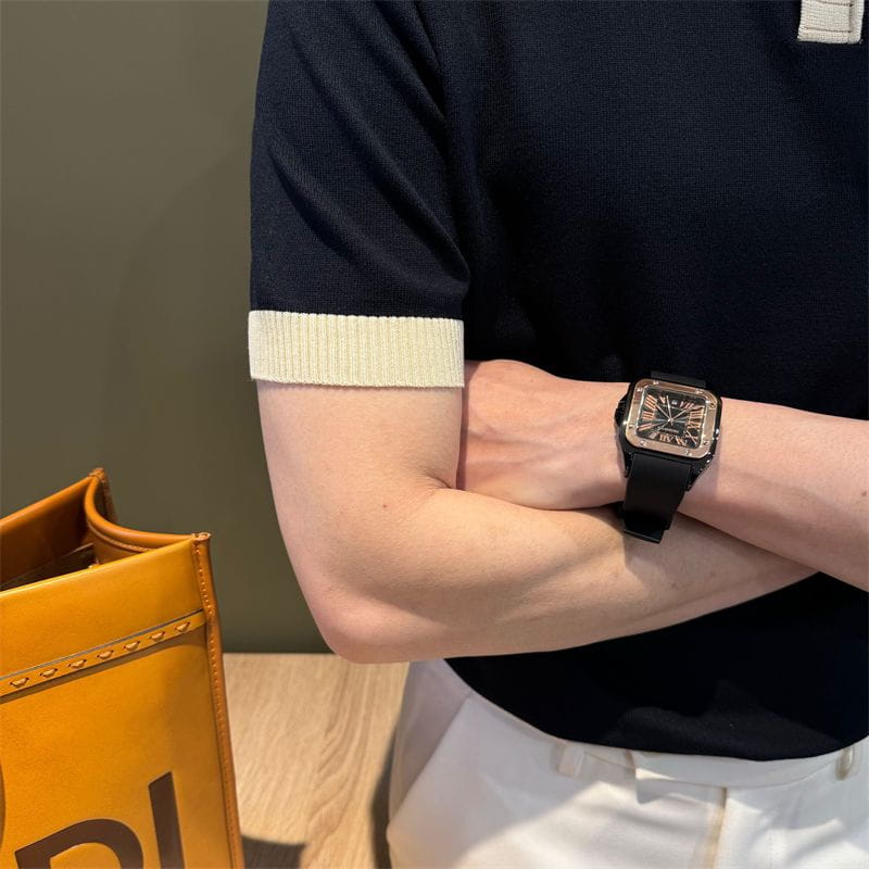Camiseta tipo polo de punto con bloques de color combinada con un reloj con correa de goma negra, con caja cuadrada, bisel color tono dorado y números romanos en su esfera oscura.
