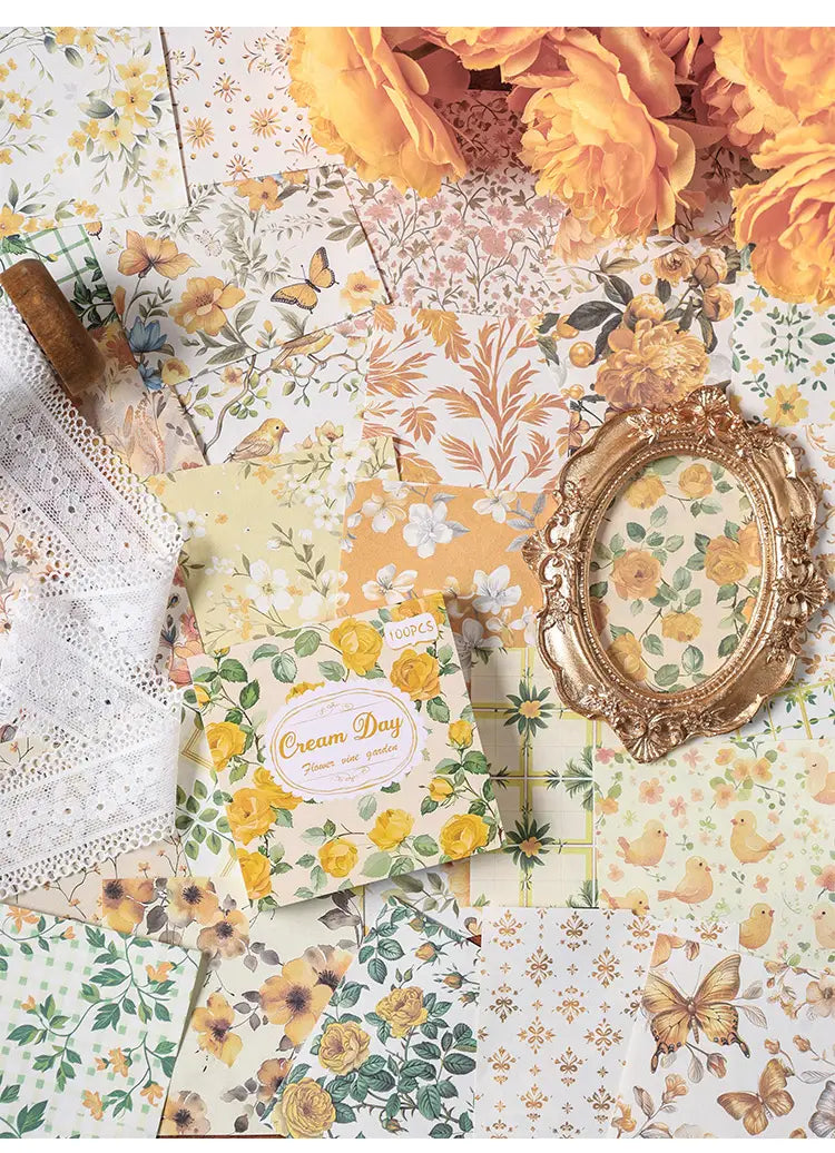 a square box of vintage scrapbooking paper and journaling supplies featuring yellow floral paper with a cream-colored oval label and assorted patterned papers with butterflies birds and roses in shades of yellow orange and green.