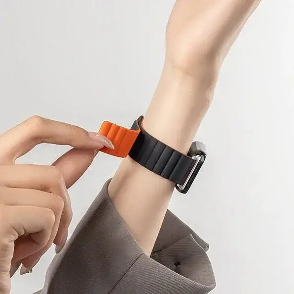 Oranges Silikon-Magnetarmband für die Xiaomi Redmi Watch mit einem schwarzen gerippten Armband und silberner Schnalle.