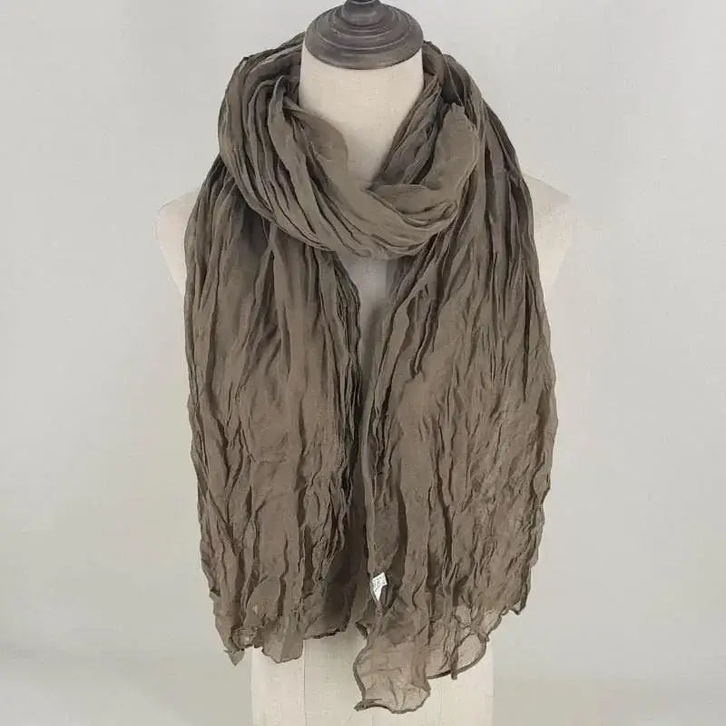 Una bufanda de algodón lino marrón topo suave y con textura para mujer, con tela ligera y transpirable arrugada, drapeada con elegancia alrededor del cuello del maniquí.