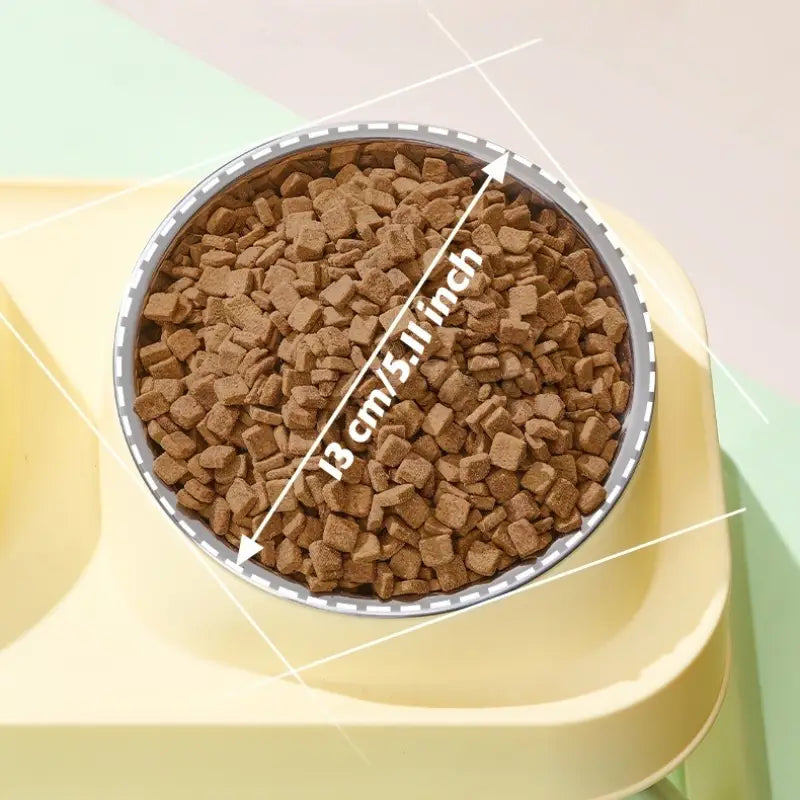 A round stainless steel pet food bowl with a silver rim filled with brown kibble in an elevated feeder with tilt bowls.