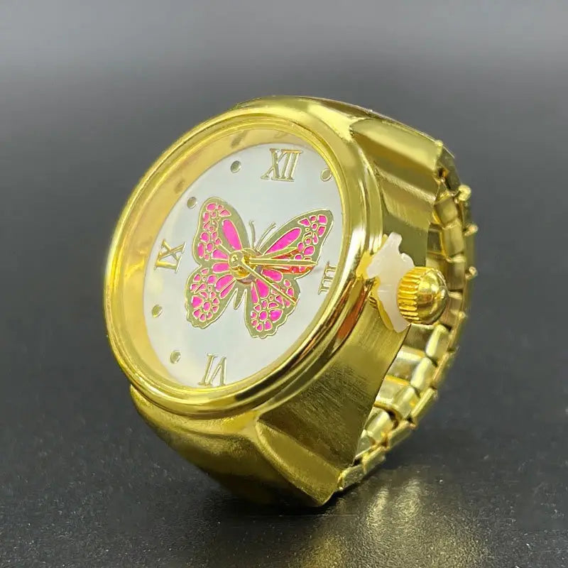 Gold-toned stainless steel butterfly watch ring with a white face featuring pink and gold butterfly design and roman numerals at the 3, 6, 9, and 12 o’clock positions.