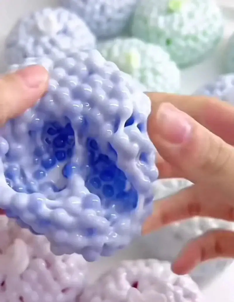 Ein durchscheinender, blau getexturter Stressball mit buckeliger, bienenwabenartig strukturierter Oberfläche und eingebetteten Gelperlen, entworfen als knisterndes Fidget-Spielzeug zur Verwendung für ASMR.