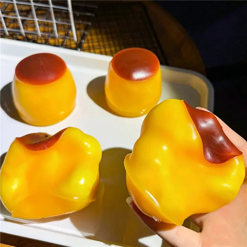 Jouet sensoriel de type balle anti-stress en forme d’arachide présentant des coupelles de dessert en gélatine jaune vif et rouge, avec des surfaces translucides brillantes.