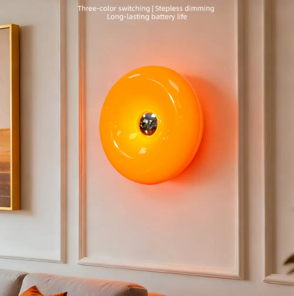 Luminaire mural tactile en acrylique orange éclatant, au format bombé laqué et à accent central métallique, avec luminosité réglable.