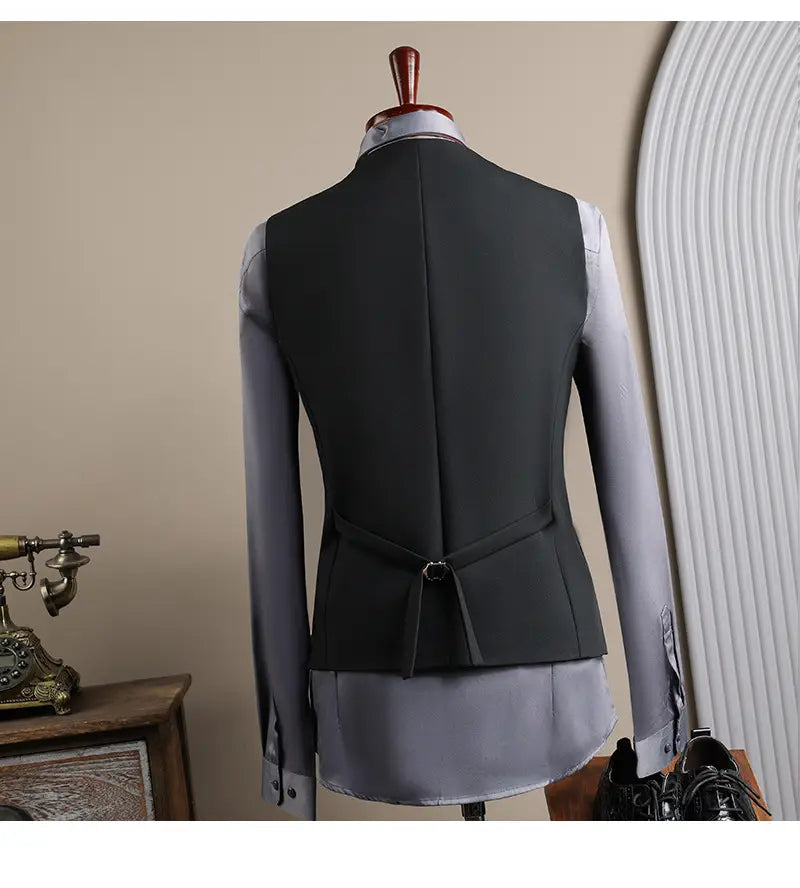 Gilet de costume pour homme noir confectionné, avec couture centrale et cravate de ceinture, porté sur une chemise habillée gris clair dans l’ensemble costume d’affaires pour homme slim fit en trois pièces, adapté aux occasions d’affaires en mode masculine et aux soirées décontractées.