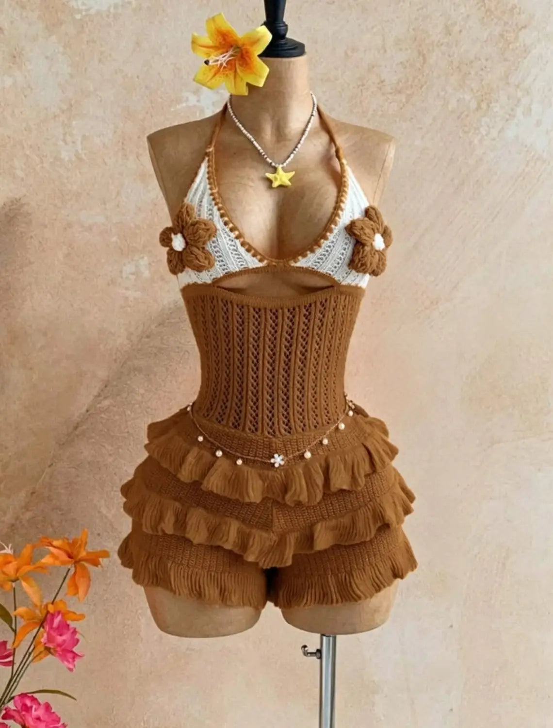 A hand-knitted white and caramel brown two-piece swimsuit with floral embellishments on the halter top and ruffled shorts featuring a delicate beaded belt in the knitted ruffle halter romper summer playsuit.