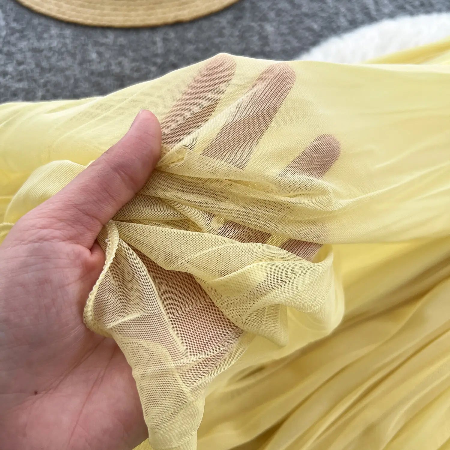 Ein blassgelber transparenter Mesh-Stoff, sanft in der Hand gehalten, für einen rosa Plisseerock Midi im A-Linien-Stil im Y2K-Streetwear.