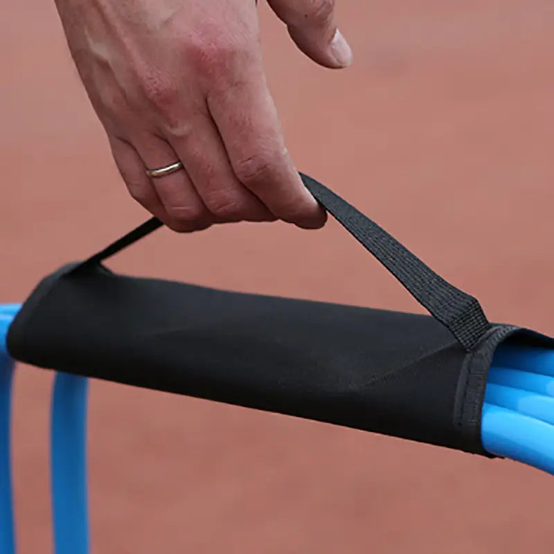 Black fabric handle cover with adjustable strap securing a blue plastic bar for a soccer agility hurdle carrying strap and storage bag.