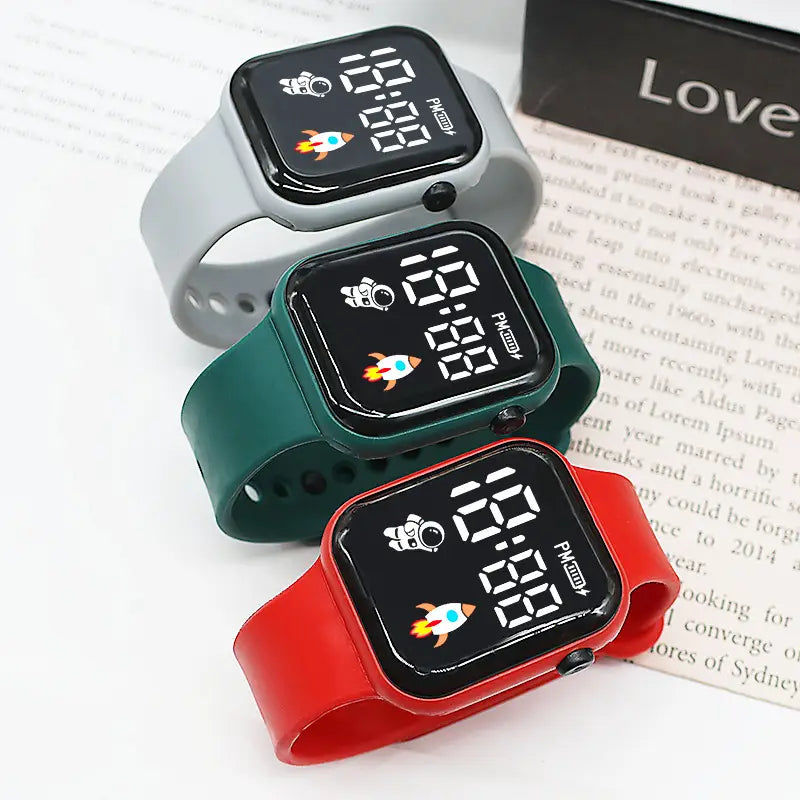 Trois montres électroniques colorées avec affichages LED à thème spatial et bracelets en silicone gris, vert et rouge, conçues pour enfants, garçons et filles.
