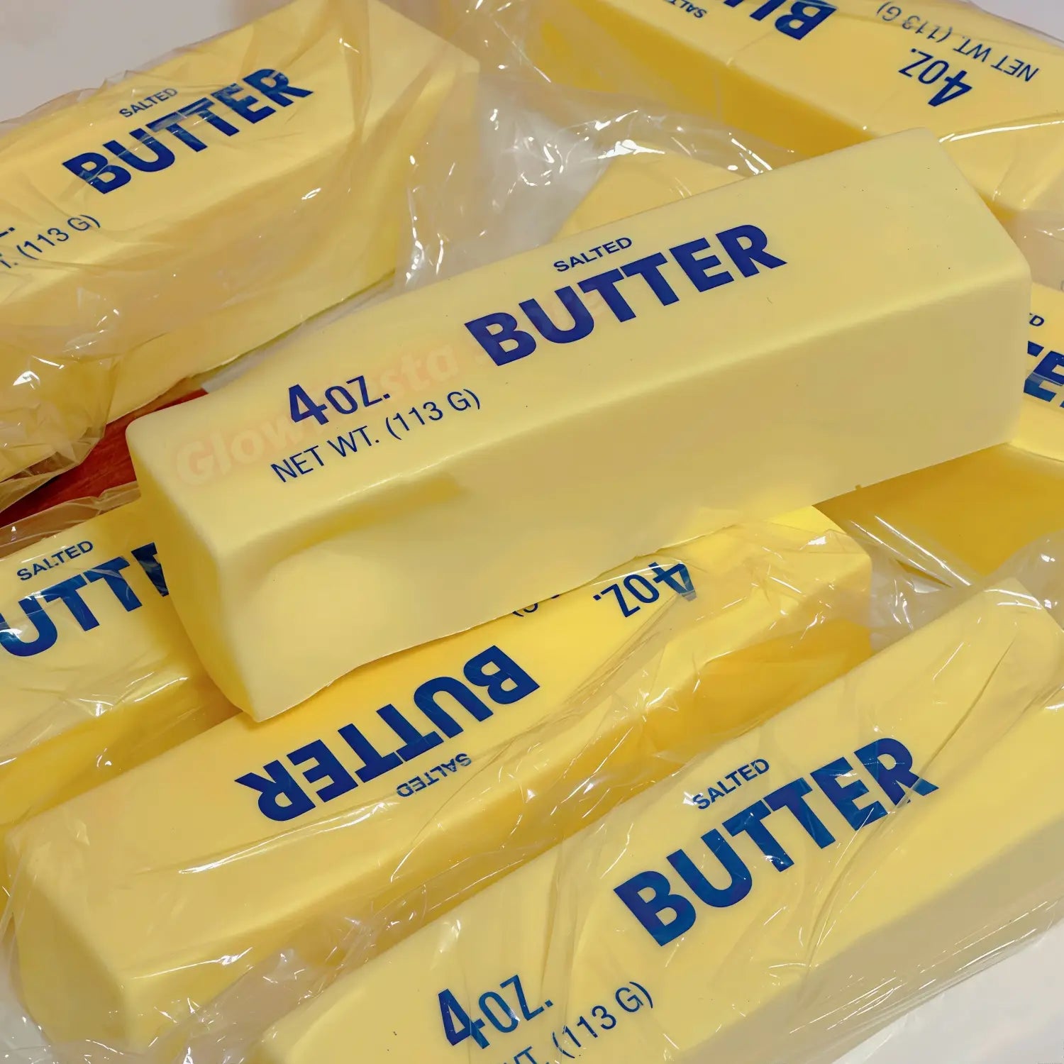 Coffret de 12 jouets antistress en bâtons de beurre salé jaunes à montée lente, chacun emballé dans un plastique transparent, avec une étiquette de marque de beurre bleu et une mention 4 oz.