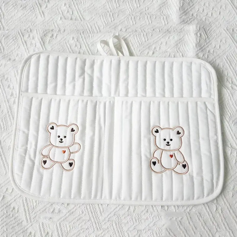 クマの刺繍が施されたキルティング製ベビーカー用オーガナイザー袋に使用するための、柔らかな布で作られた白いキルティングのベビーおむつ替えシートで、黒と赤のハートが描かれた刺繍のテディベアが2匹付いています。