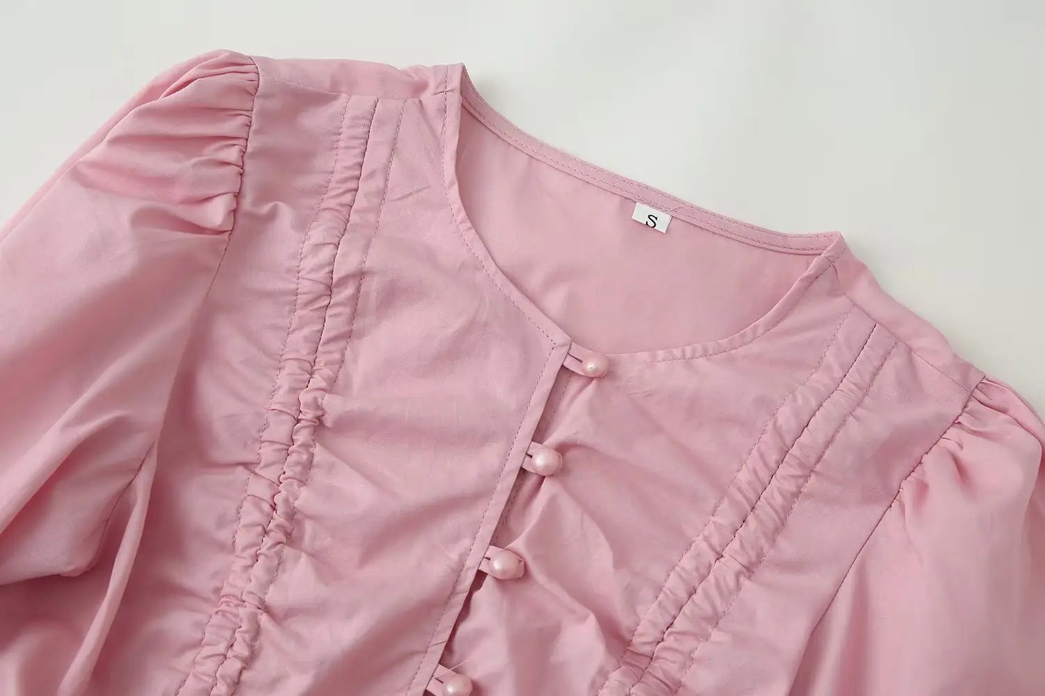 A soft pink satin-like women slim fit long sleeve top with a round neckline featuring gathered puffed sleeves and delicate ruched detailing along the front placket.