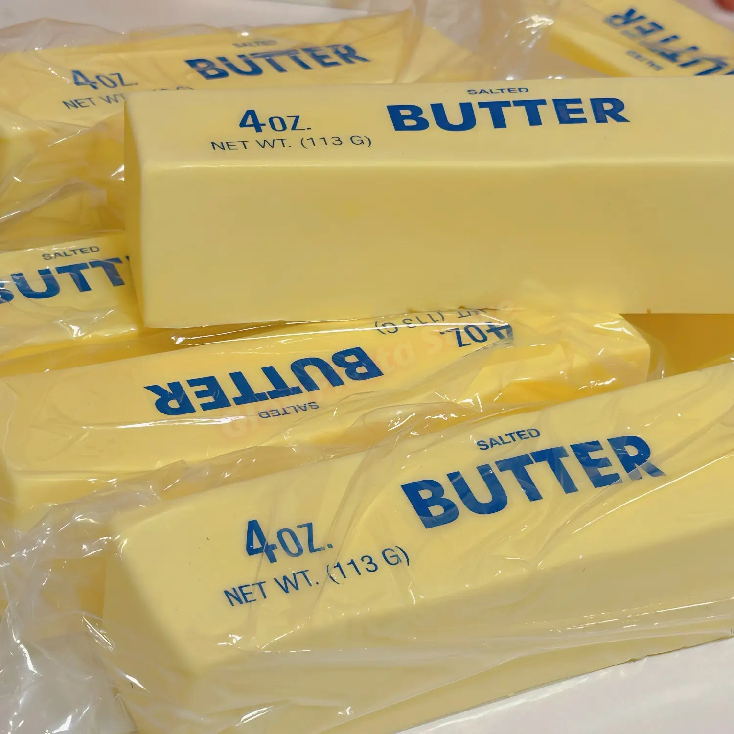 Coffret de 12 jouets antistress en bâton de beurre jaune à montée lente, chaque bâton étant emballé dans un plastique transparent, avec une étiquette de marque de beurre bleu et indiqué comme pesant 4 oz.