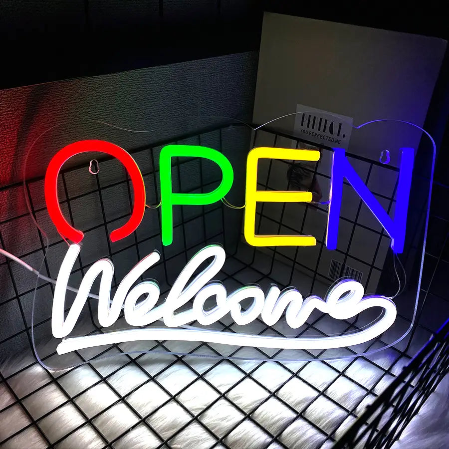 Une enseigne néon vibrante de couleur arc-en-ciel, alimentée par USB, avec le mot « ouvert » en lettres majuscules grasses, et « bienvenue » inscrit en script en dessous.
