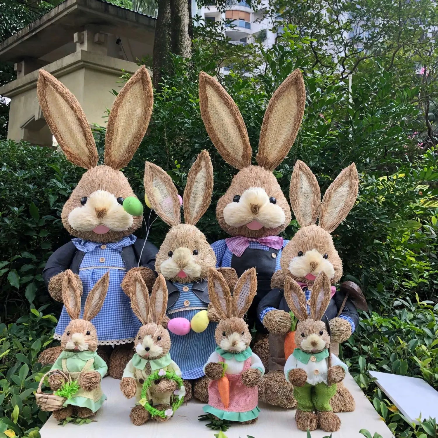 A family of eight rustic straw-textured 35cm Easter rabbit figurines dressed in coordinated outfits with oversized ears and embroidered details.