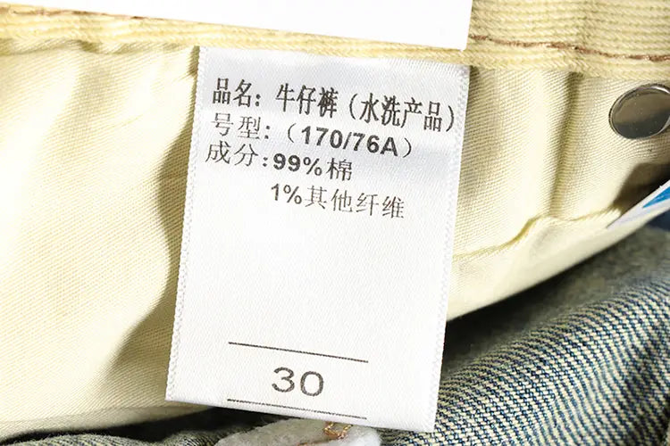 Une étiquette blanche d’entretien du tissu cousue dans la ceinture des jeans en denim ample à broder en denim clair pour hommes, indiquant par un texte chinois que le produit est lavé à l’eau et composé de 99 pour cent de coton.