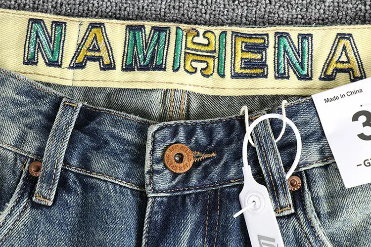 Jeans en denim bleu ample pour hommes avec une ceinture beige comportant une broderie Namihena en lettrage vert et jaune.