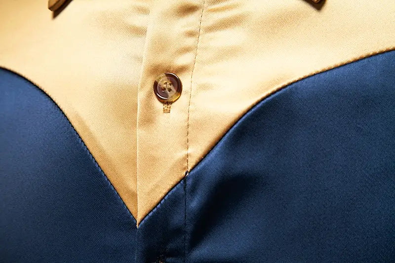 Ein Herrenhemd mit goldfarbenem Besatz aus Satin mit einem goldfarbenen Knopf mit leichtem Schimmer am Kragen auf glattem navyblauem und beigem Satinstoff.
