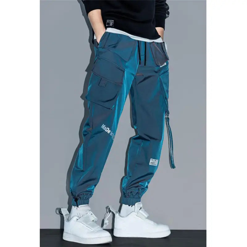 Teal mens tactical cargo pants in reflective material with multiple pockets and a drawstring waistband designed for streetwear.