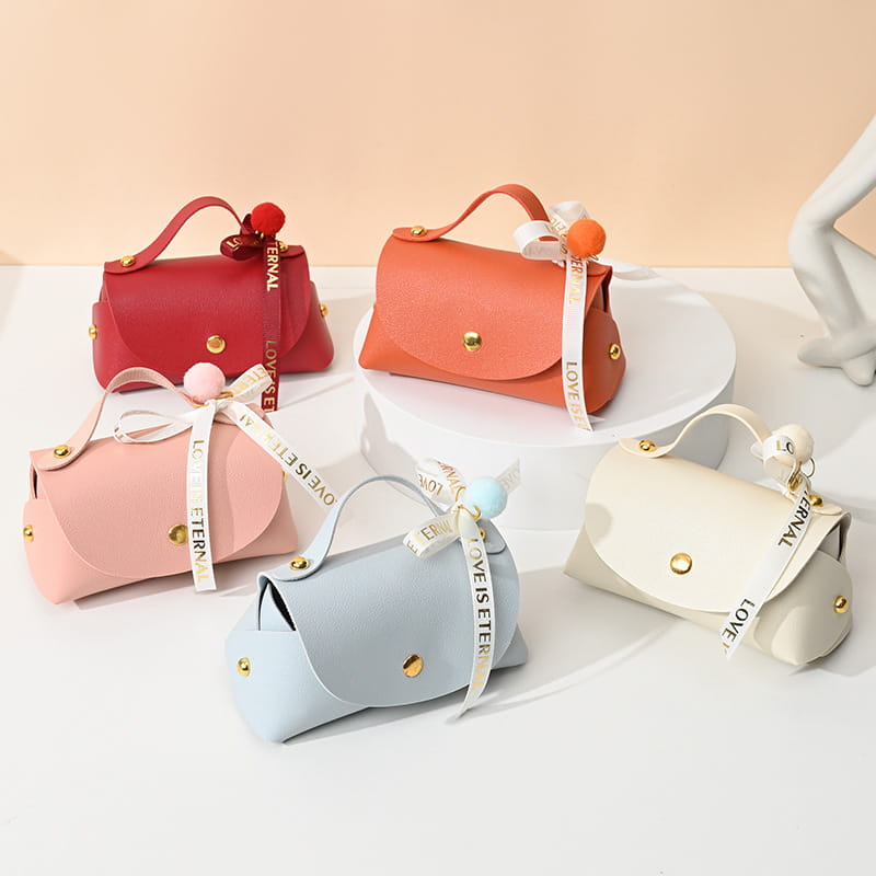 Sac cadeau de mariage en cuir, mini pochette, en couleurs pastel, fabriqué dans une matière douce à l’aspect cuir avec des ornements de quincaillerie ton or et des rubans décoratifs noués autour des anses.