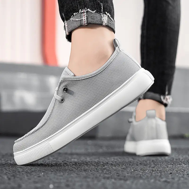Chaussures de type mocassins décontractées pour hommes, modèle à enfiler en toile en maille grise, avec semelle en caoutchouc blanc et œillets noirs.