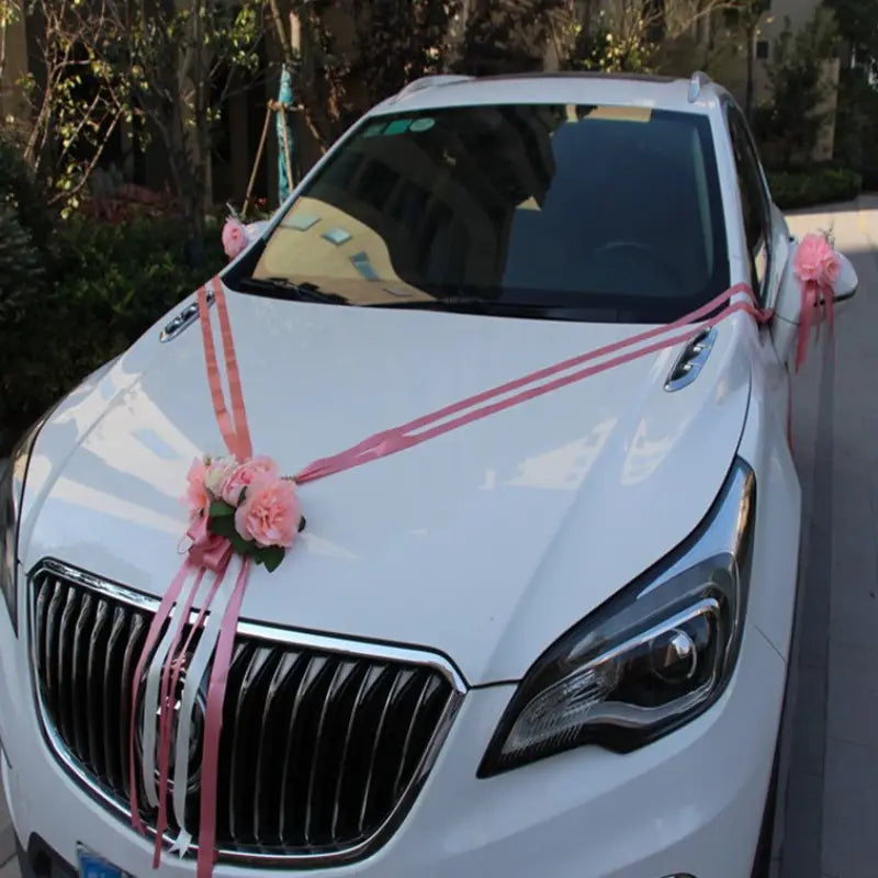 Voiture de mariage Buick Envision blanche décorée de rubans de fleurs artificielles roses et blancs provenant de l’ensemble de décoration florale artificielle pour voiture de mariage.