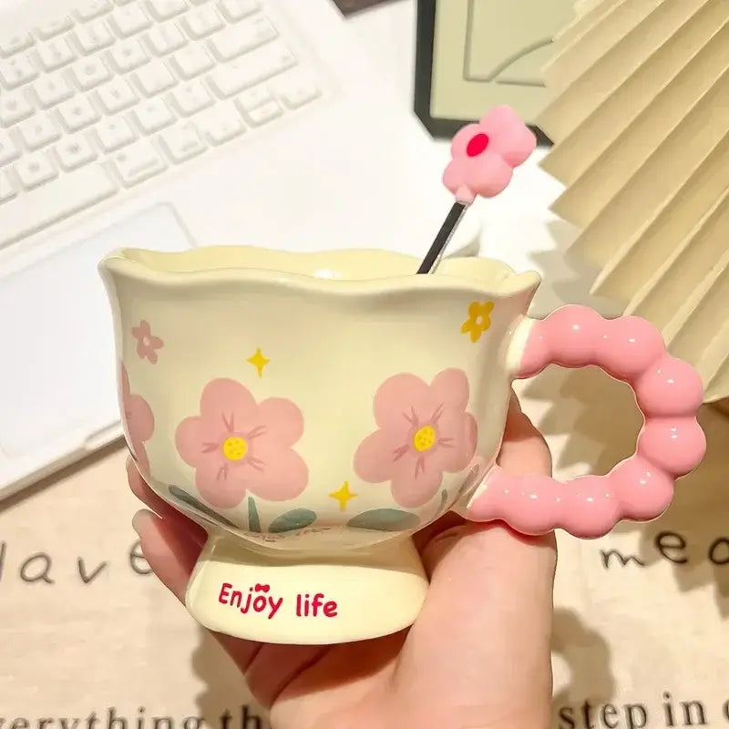 Une tasse à thé en céramique tulipe rose pastel et crème, avec un bord festonné, des fleurs roses peintes à la main avec des cœurs jaunes et des feuilles vertes, accompagnées d’une cuillère assortie en forme de fleur rose, le tout dans la boîte cadeau en céramique tulipe à motif floral.