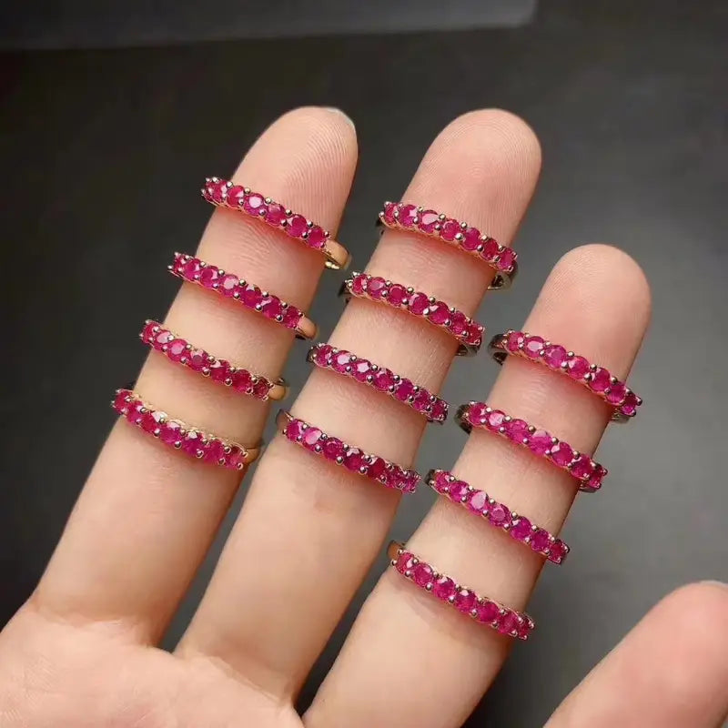 金調の留め具と鮮やかな赤色の宝石があしらわれた、繊細な天然ルビーのシルバーリングバンド9点セットが重ねて配置されています。