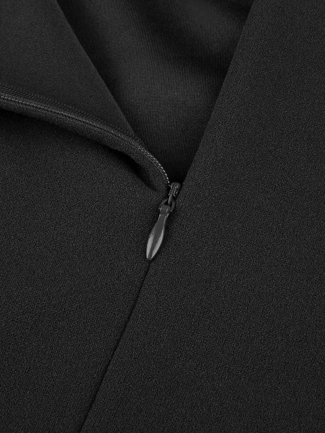 Jupe de travail mi-haute plissée noire présentant une fermeture éclair noire avec une languette métallique élégante sur un tissu foncé.