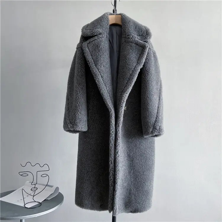 Abrigo exterior tipo osito de peluche largo para mujer de lana color gris medio, con textura esponjosa suave y cuello ancho, colgado en una percha de madera; destaca los detalles relevantes para las mediciones del contorno de pecho y del contorno de cadera, así como consultas del servicio de atención al cliente.