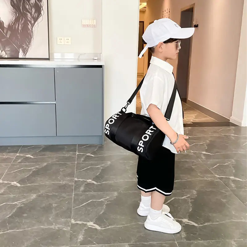Schwarze zylindrische Kinder-Sport-Reise-Sporttasche mit weißer Sportbeschriftung und verstellbarem schwarzem Riemen für Reise-, Gym- und Crossbody-Gepäck.