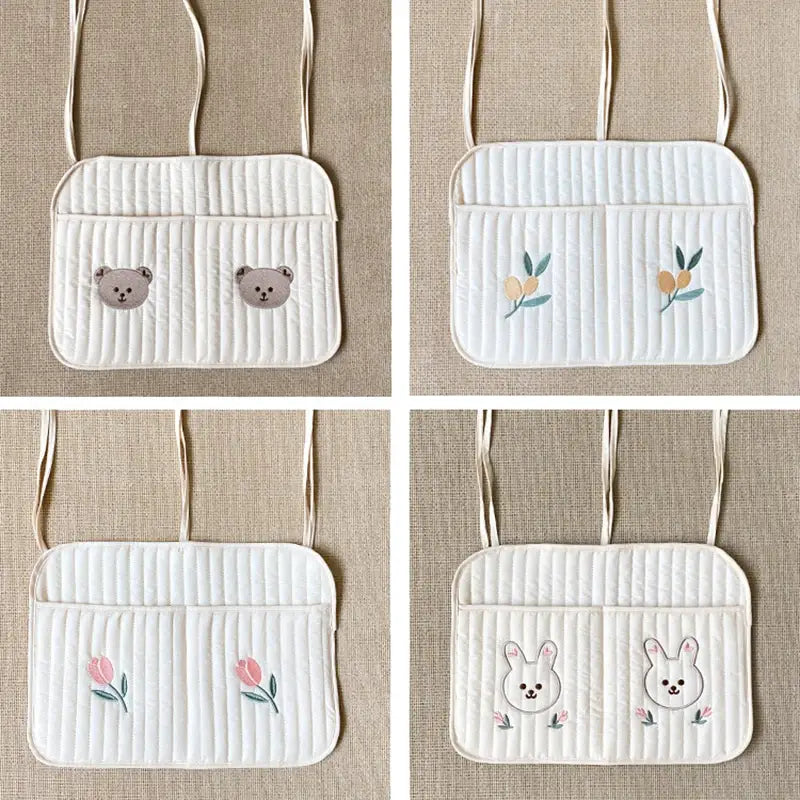クマの刺繍が施された白いキルティング製ベビーカー用オーガナイザー袋で、動物と花のデザイン、そしてそれに合わせたストラップが付いています。
