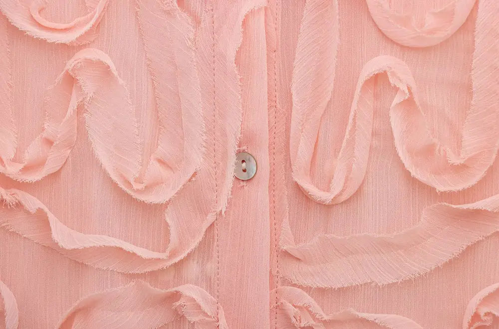 A delicate pink textured ruffled button up blouse with a subtle sheen and a single silver button at the center.