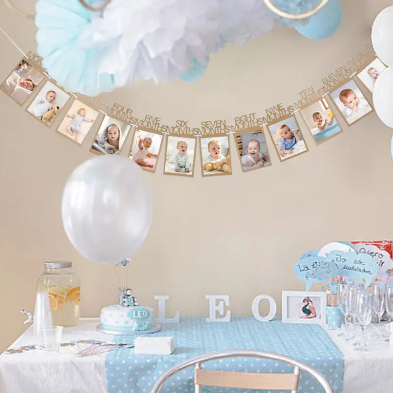 A 1st birthday photo banner featuring gold-colored frames and printed photos of a child at various ages strung across the wall as a monthly picture garland.
