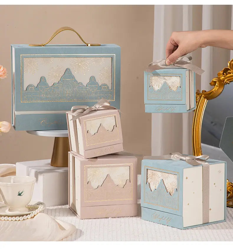 pastel blue and beige european style wedding gift box candy packaging with gold-trimmed mountain cutouts and satin ribbon ties