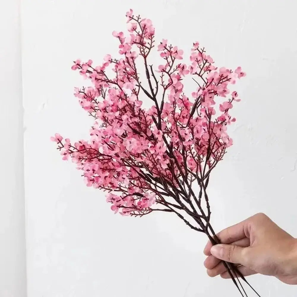 a delicate bouquet of artificial flowers cherry blossoms in pink with dark brown branches held together by a hand