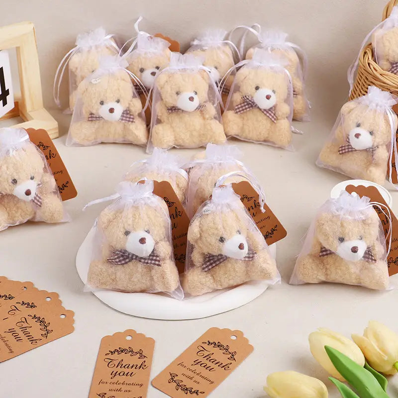 茶色と白のチェック柄のリボン付きのベージュのぬいぐるみテディベアのお祝品を、オーガンジー袋付きのテディベアのお祝品セットとして、透明なオーガンジー袋に包装しています。