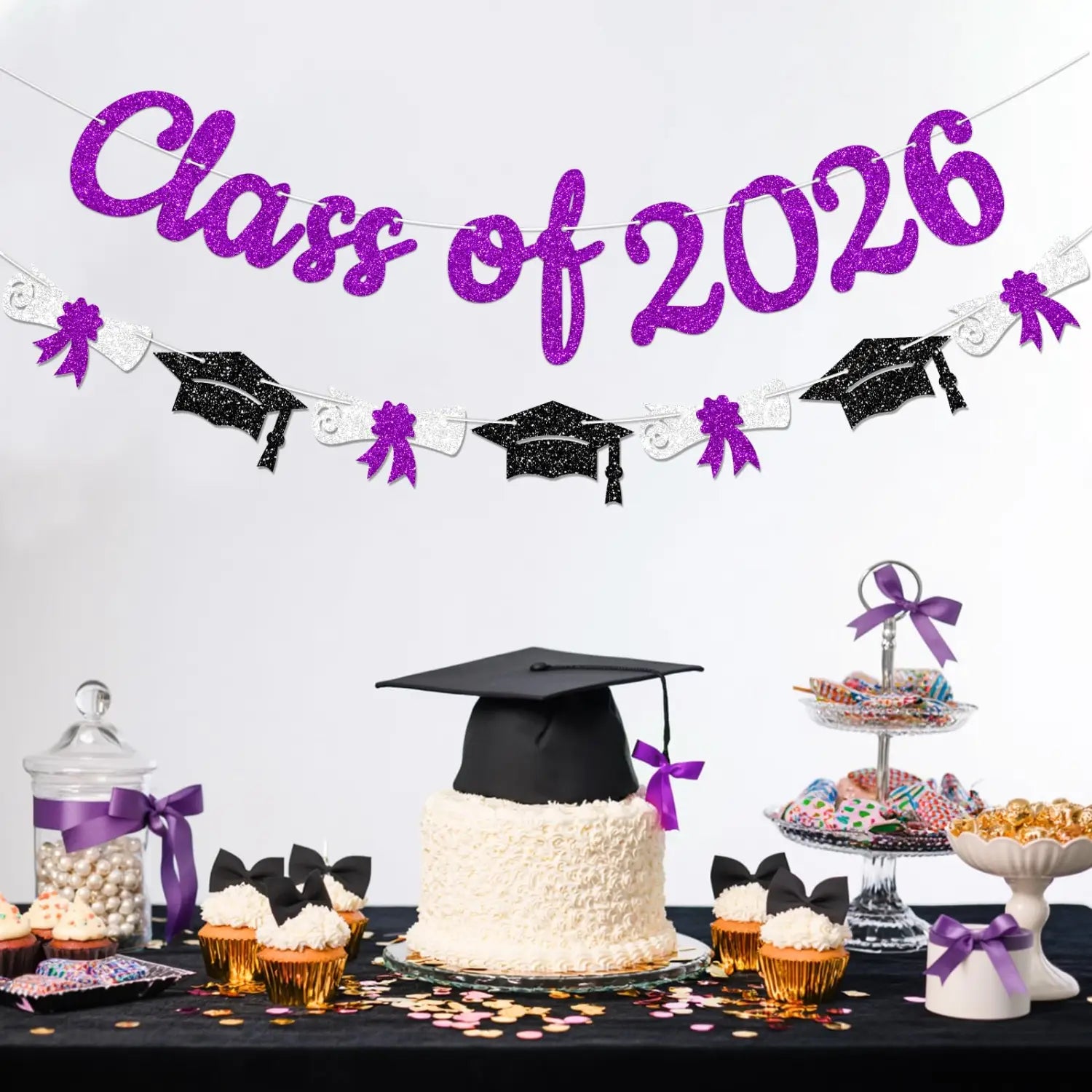 A class of 2026 graduation banner and garland featuring a black graduation cap with a purple ribbon on a white textured cake.