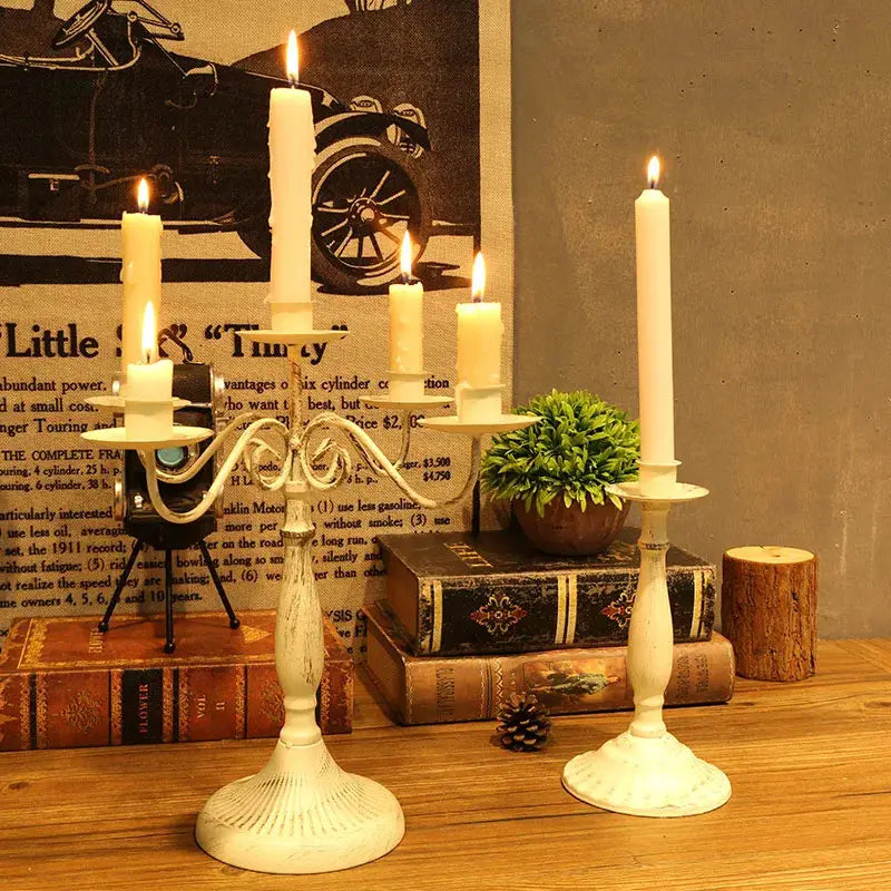 porte-bougies en métal blanc vieilli, avec un décor de volutes ornementales et quatre bougies allumées de couleur crème, pour des décorations de table, décoration moderne et européenne, mariage d’hôtel.